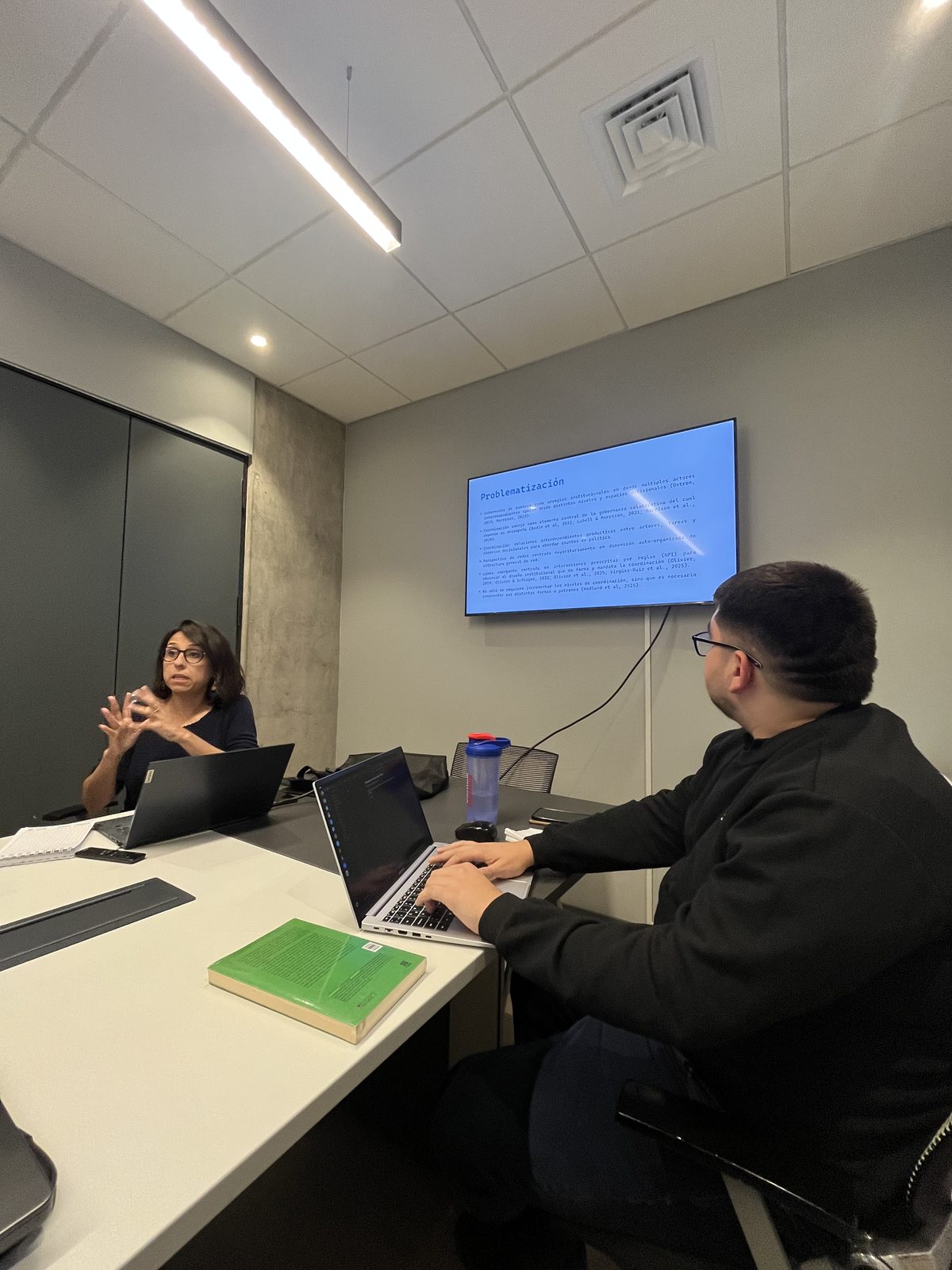 Two group members in a meeting room discussing a presentation shown on a wall screen