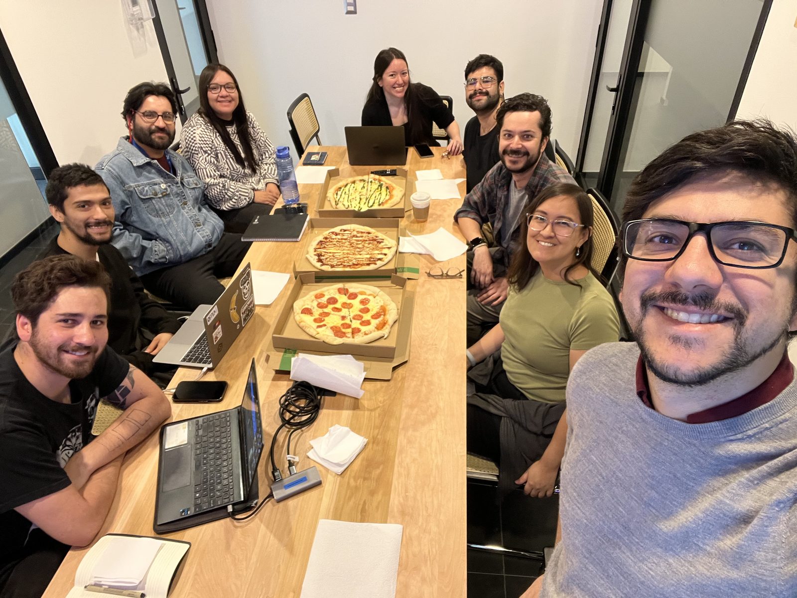 Group members smiling around a table with laptops and pizza boxes